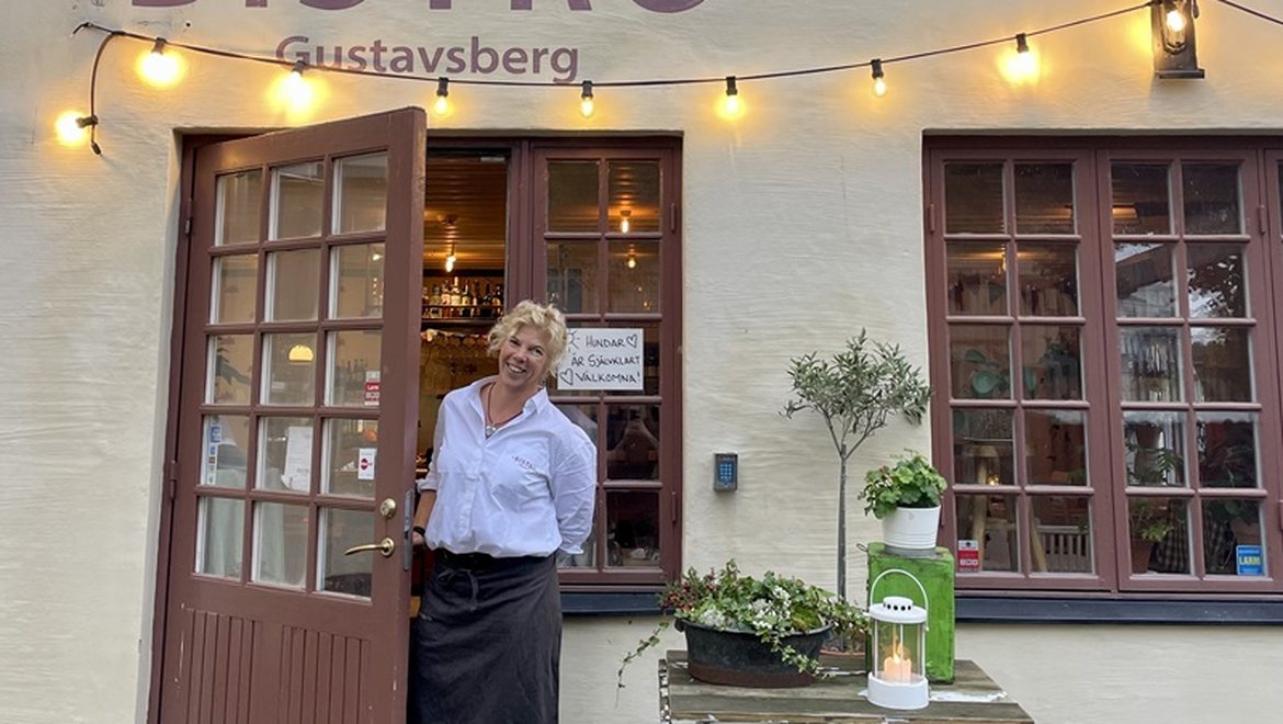Värd i dörröppningen till Bistro Gustavsberg, varmt kvällsljus.